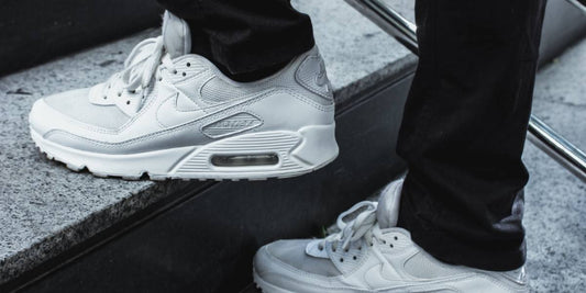 Persoon die witte Nike Air Max 90 draagt terwijl hij op een trap loopt